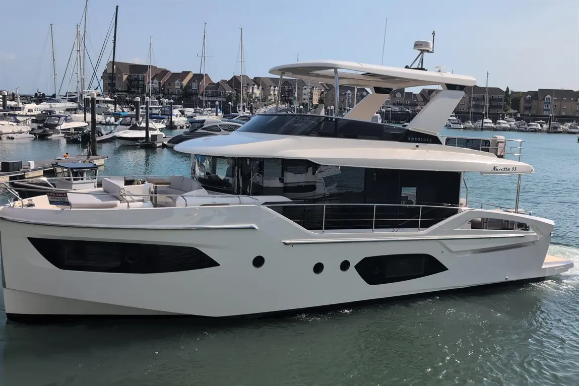 A sleek white motor yacht, "Nebula 53," docked at a marina with other boats in the background. A "For Sale" sign is visible.